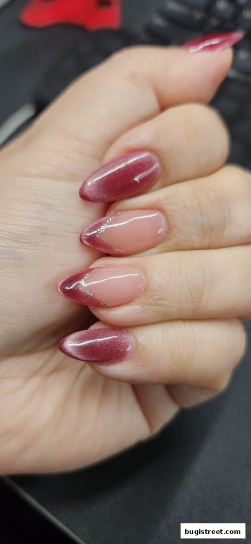 Close-up of a hand with almond-shaped nails featuring a French manicure with a glitter accent.