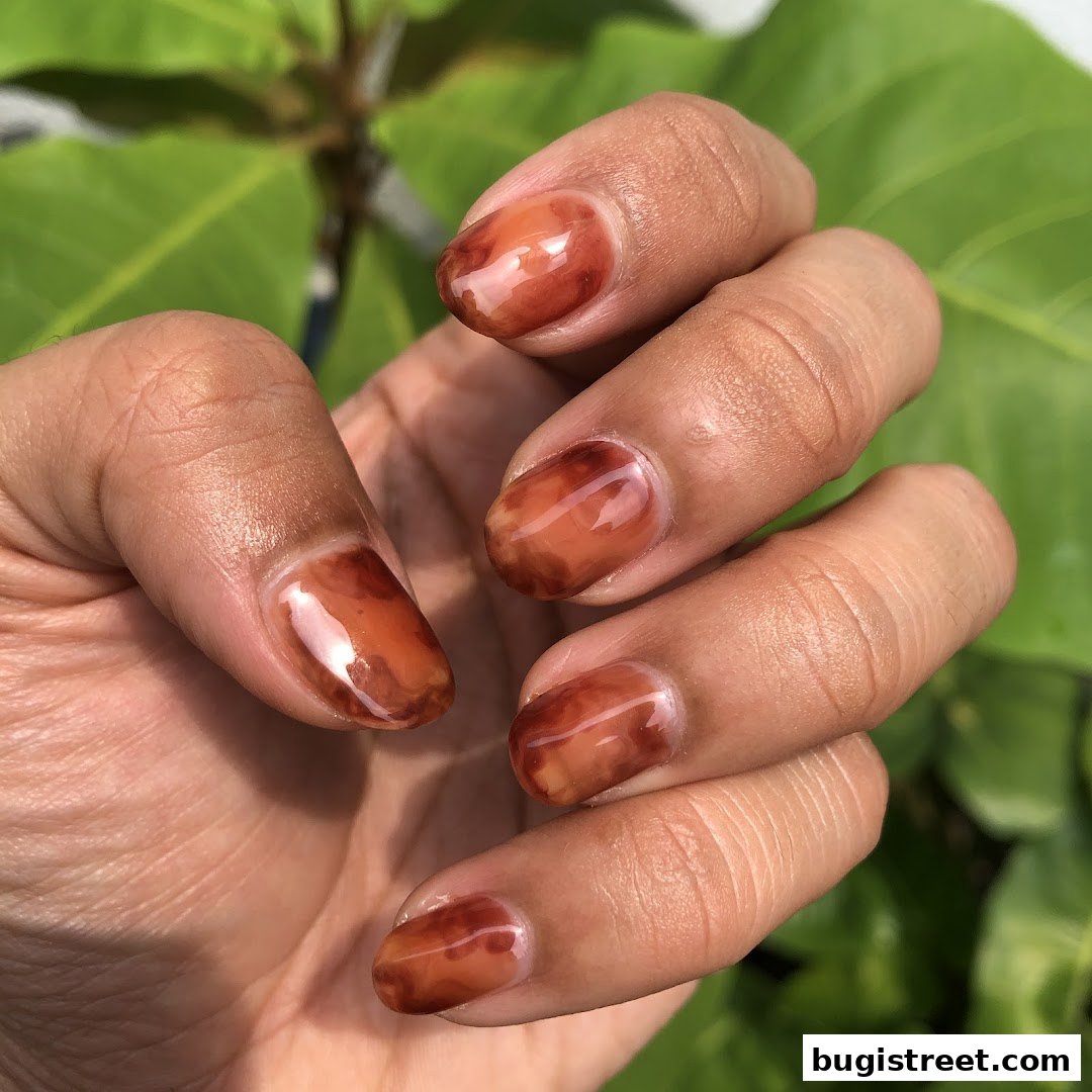 A close-up shot of a hand with beautifully manicured nails featuring a unique brown marble design.