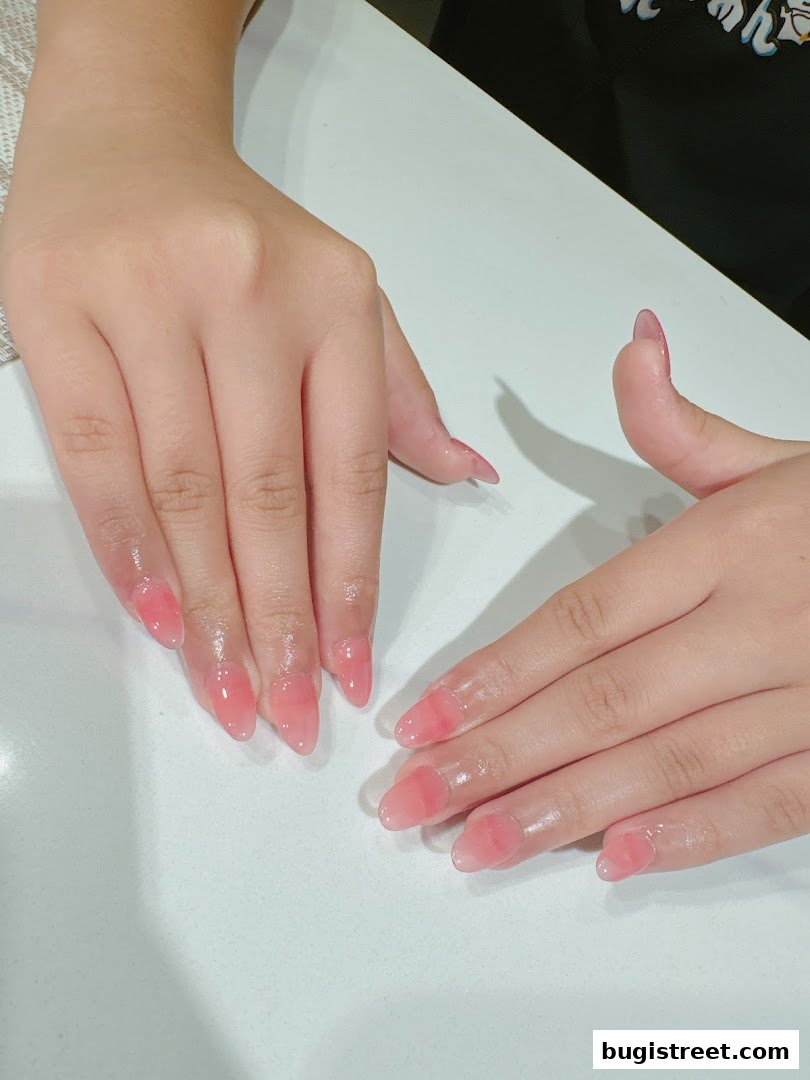 Close-up of hands with beautifully manicured, translucent pink gradient almond-shaped nails.