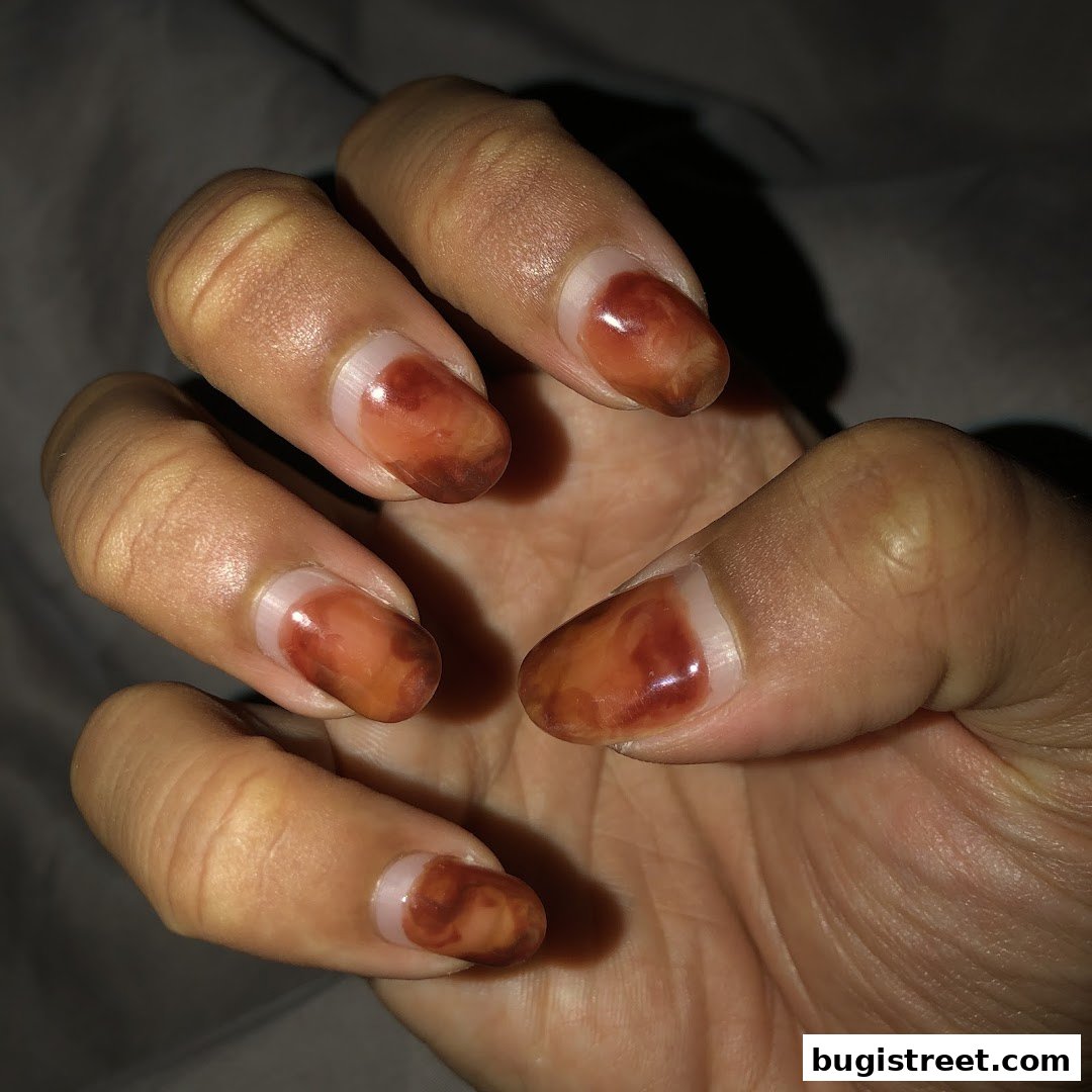 A close-up shot of a hand with almond-shaped nails featuring a marbled brown and clear polish design.