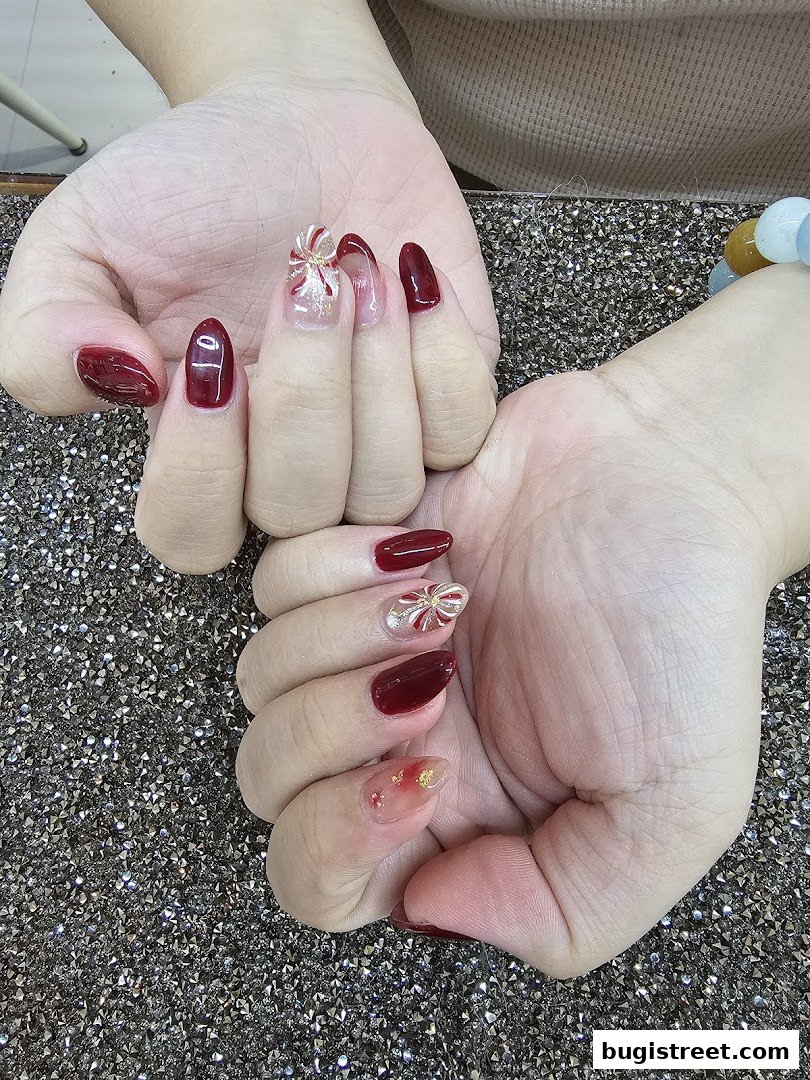 Close-up of hands with beautifully decorated nails in a deep red shade with intricate designs.