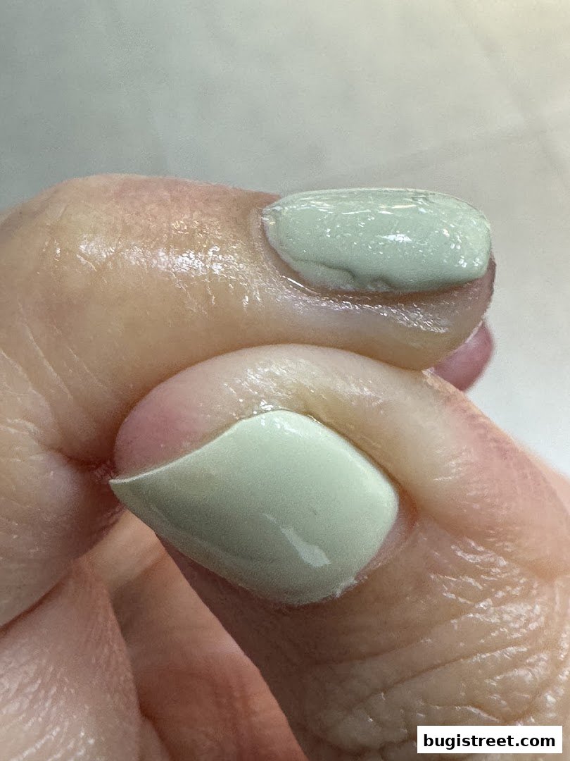 Close-up of a hand with light green nail polish applied to two fingernails.