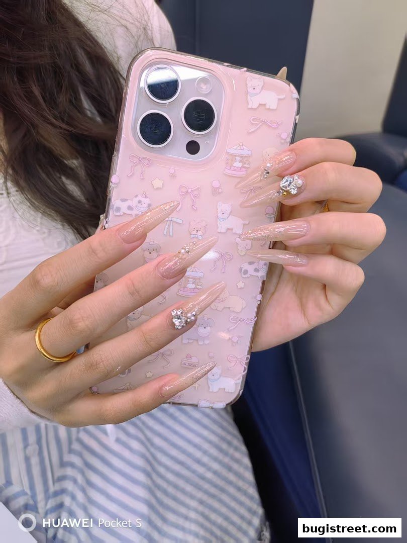 A person displays long, elegant nails adorned with rhinestones and pearls, holding a phone case with cute cartoon designs.
