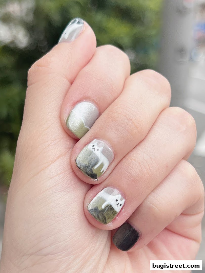 A close-up of a hand with artistic nail art featuring white cats on a green and grey background.