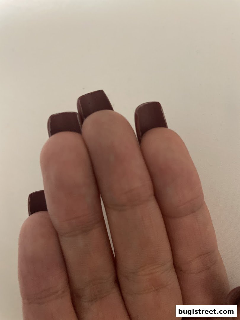 Close-up of a hand with perfectly manicured, square-shaped nails painted in a deep burgundy color.