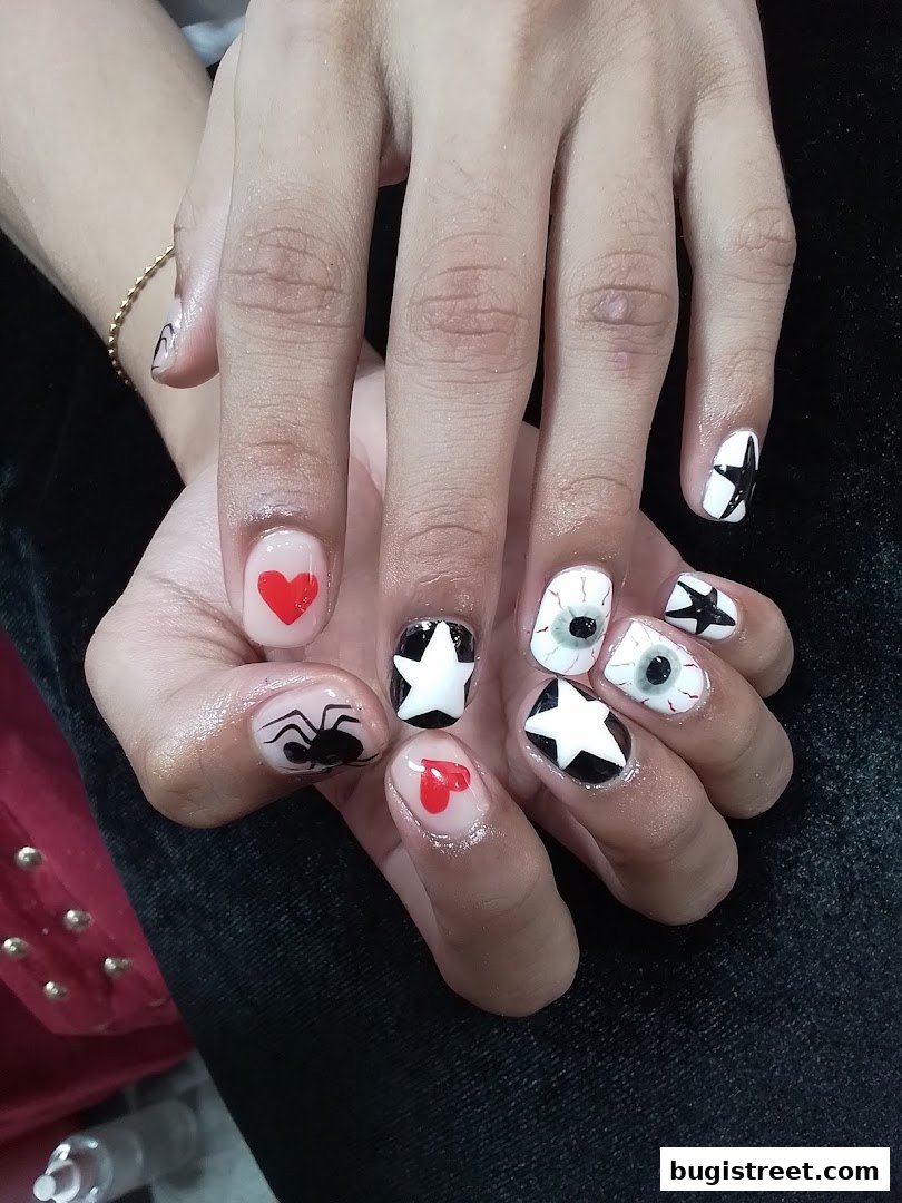 A close-up of hands with creative Halloween-themed nail art, featuring spiders, hearts, stars, and eyeballs.
