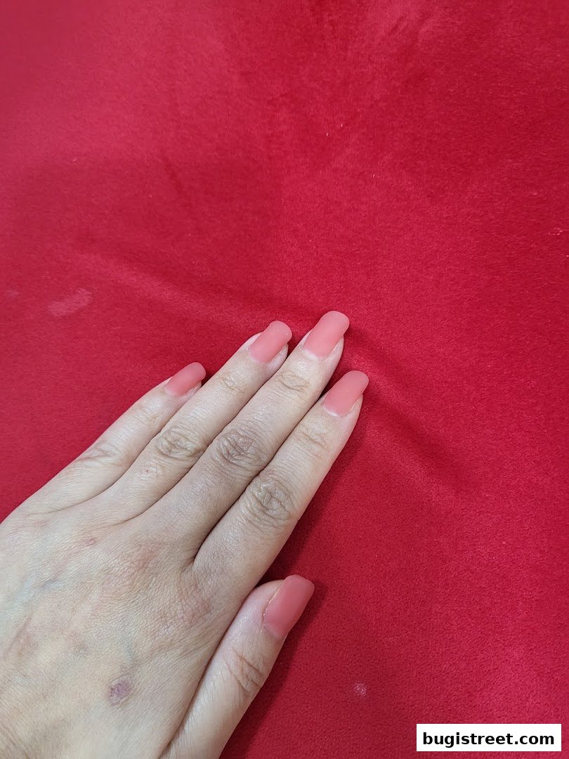 A hand with neatly manicured coral-colored nails rests on a vibrant red textured surface.