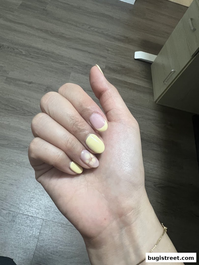 A close-up of a hand with light yellow French tip and floral accent nails.