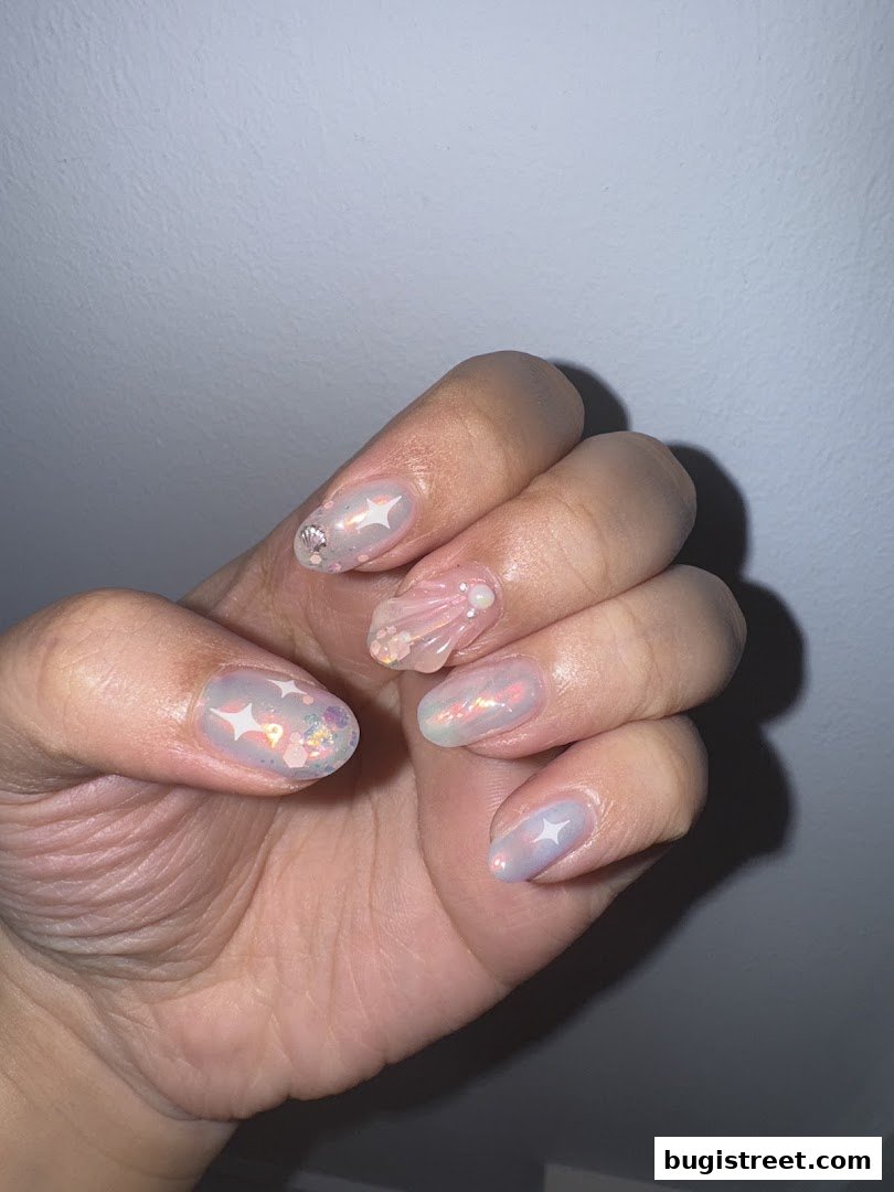 A hand with beautifully decorated nails featuring a pearlescent finish and celestial-themed embellishments.
