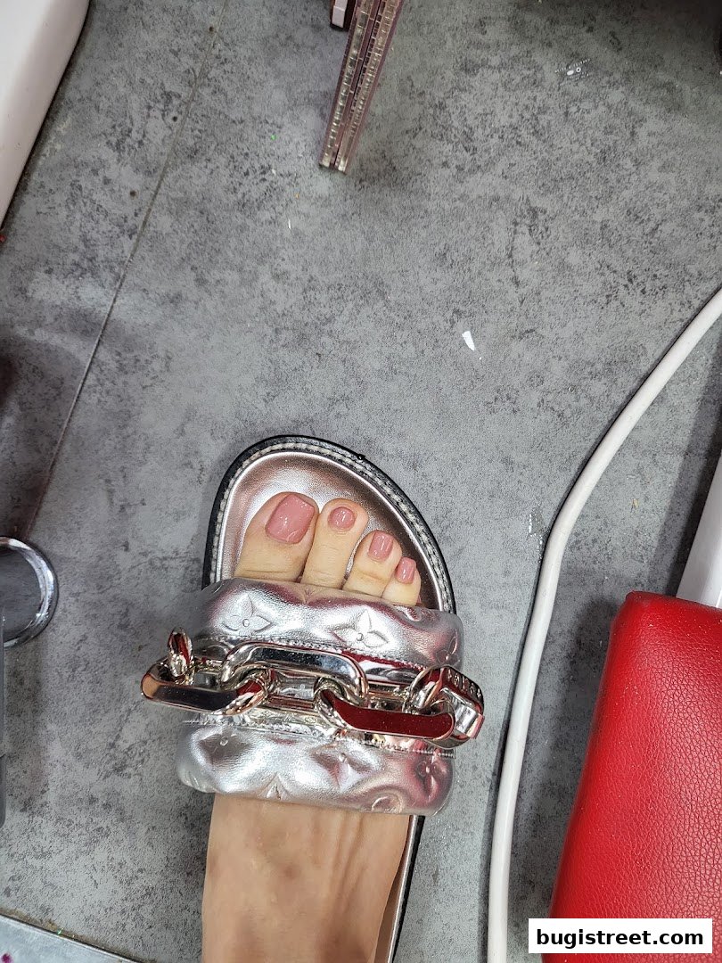 A close-up of a person's foot with a stylish silver sandal featuring a prominent chain detail.