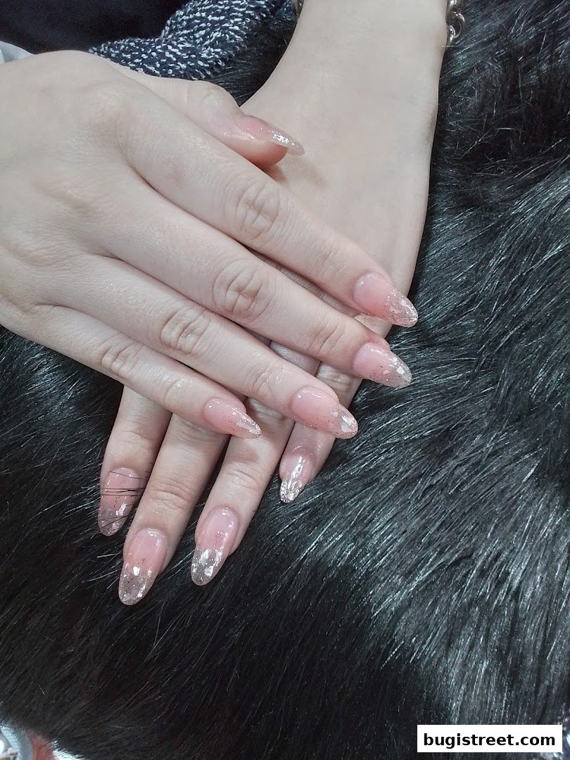 Close-up of a person's hands with elegant, long, almond-shaped nails adorned with glitter.