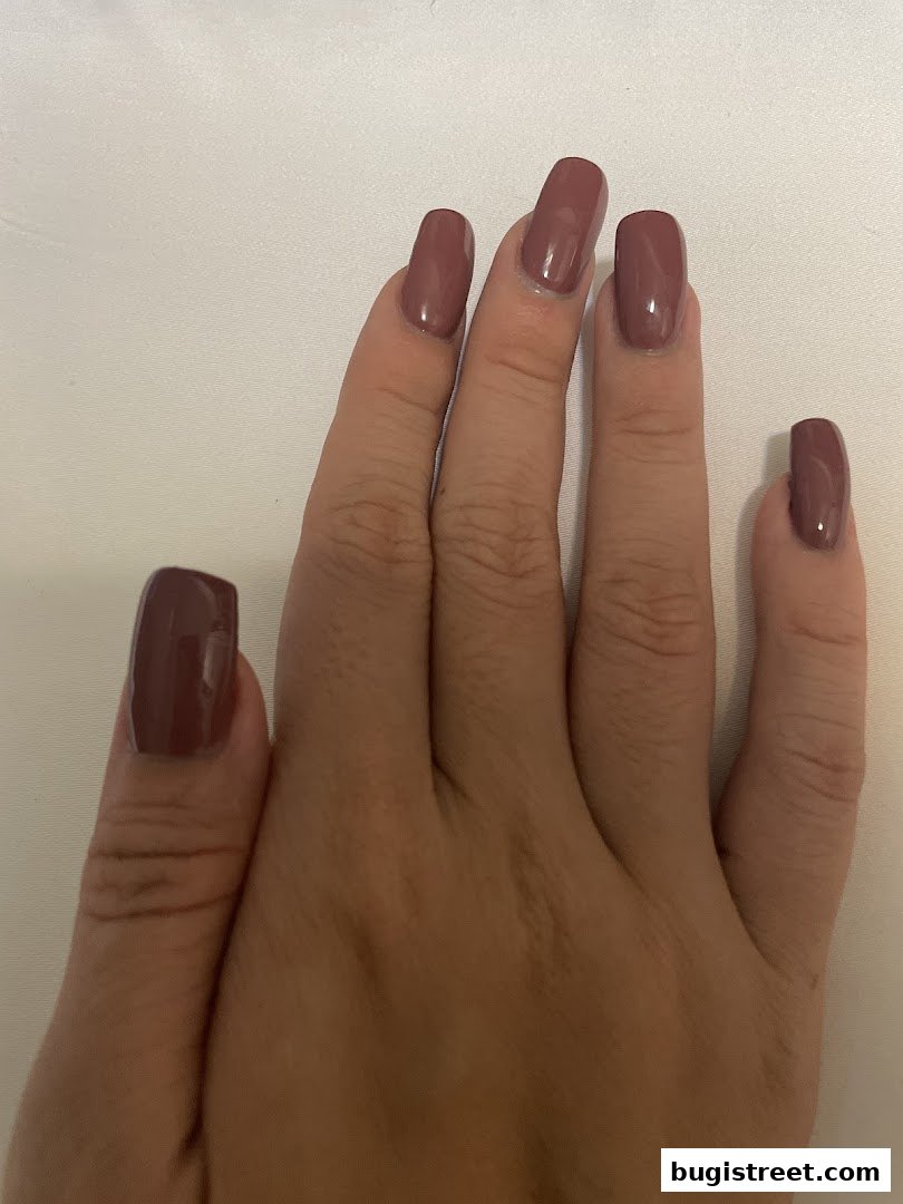 A close-up of a hand with perfectly manicured, square-shaped nails painted in a muted mauve shade.