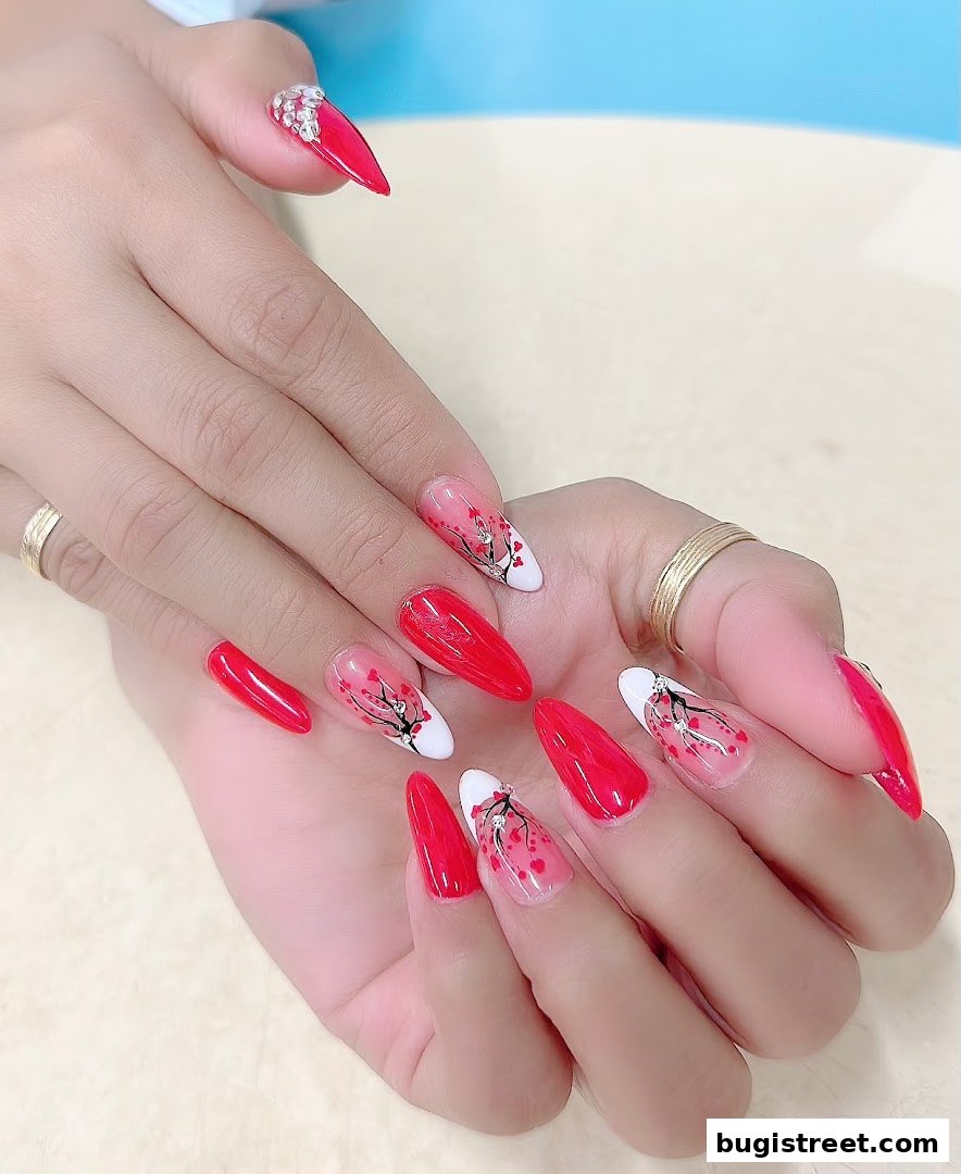 A close-up of hands with beautifully designed red and white almond-shaped nails with cherry blossom art.