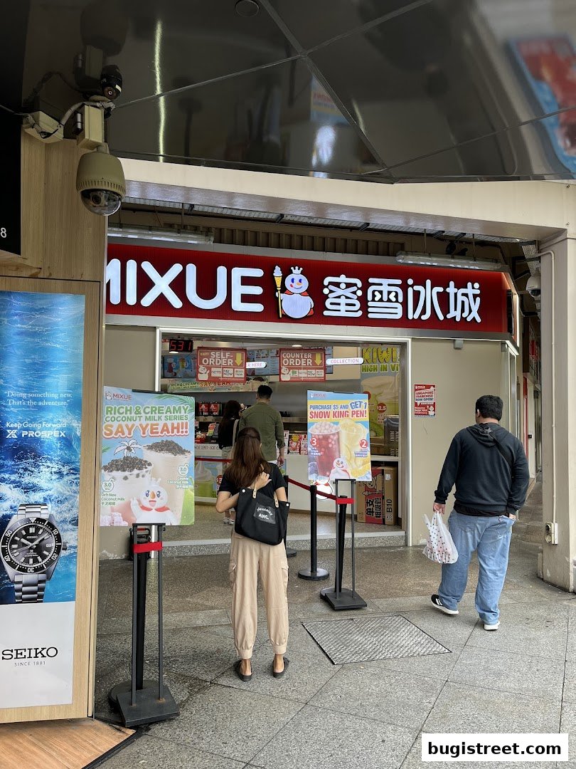 People queuing outside a MIXUE ice cream and tea shop with promotional posters.