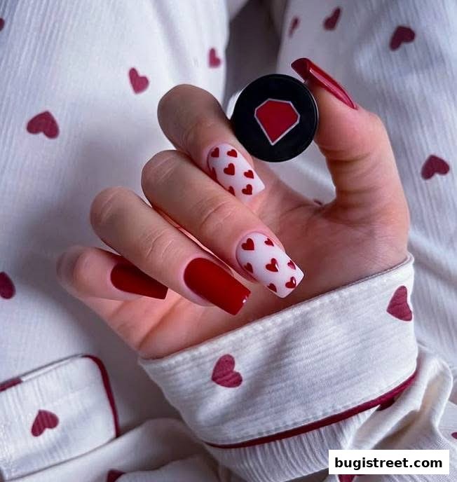 A hand with red and heart-patterned nails holding a small black container with a red diamond logo.