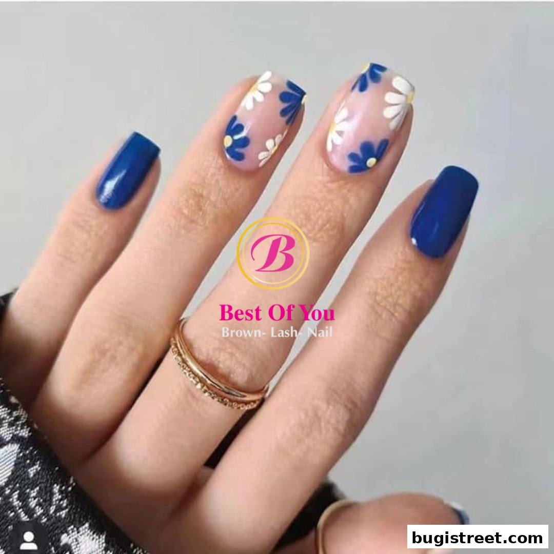 A close-up of a hand with beautifully manicured nails, featuring floral designs and solid blue polish.