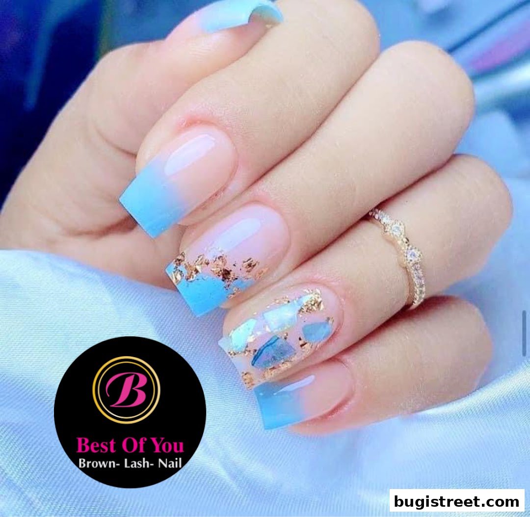 A close-up of a hand with beautifully decorated nails featuring blue ombre and gold accents.