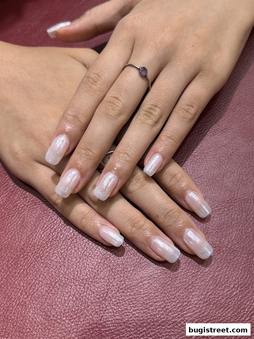 Close-up of hands with perfectly manicured, pearlescent white nails and a delicate ring.