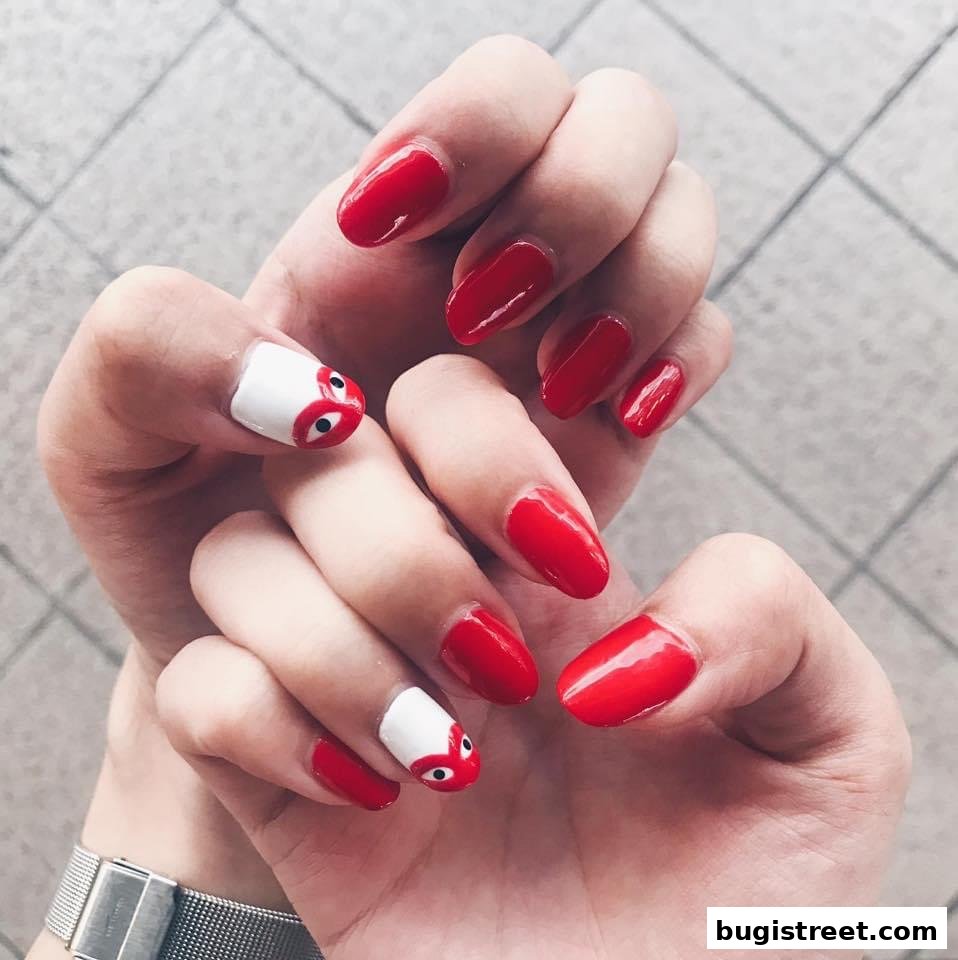 Close-up of hands with vibrant red gel nails and two accent nails with a white base and a cute cartoon eye design.