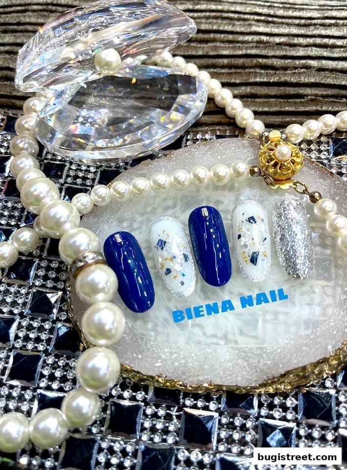 A display of five nail art samples with blue, white, and glitter finishes, adorned with pearls.