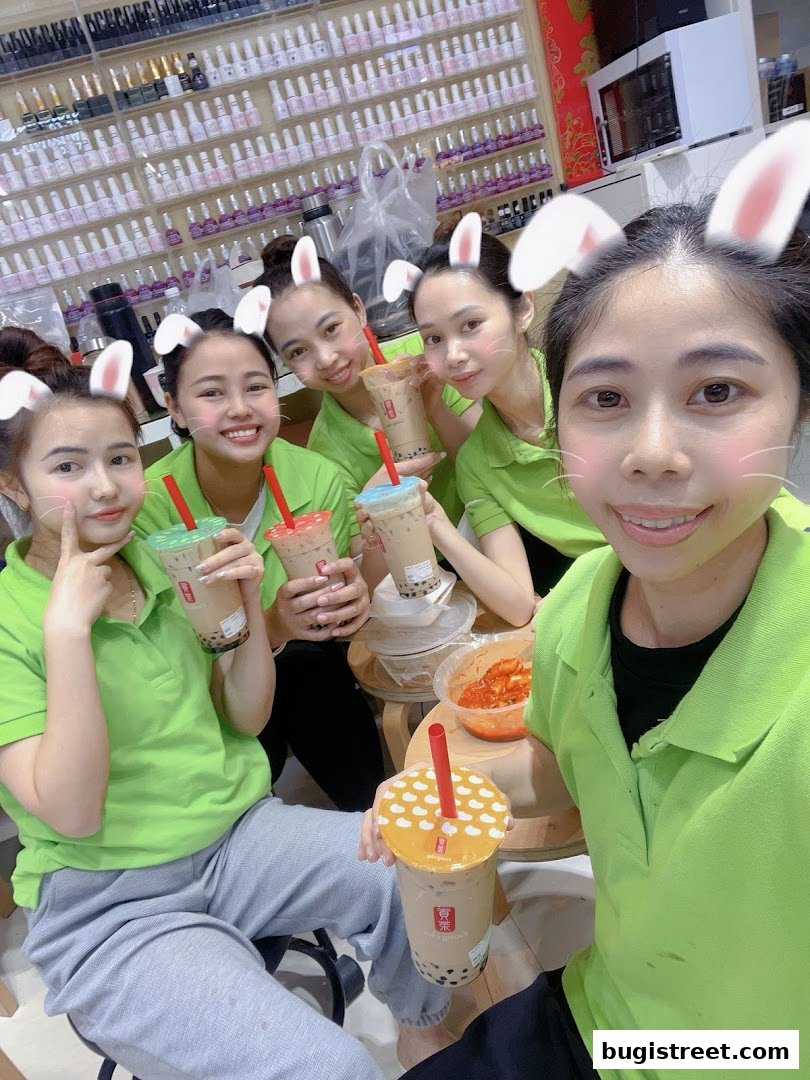 Five smiling women in green shirts with bunny ears holding bubble tea drinks.