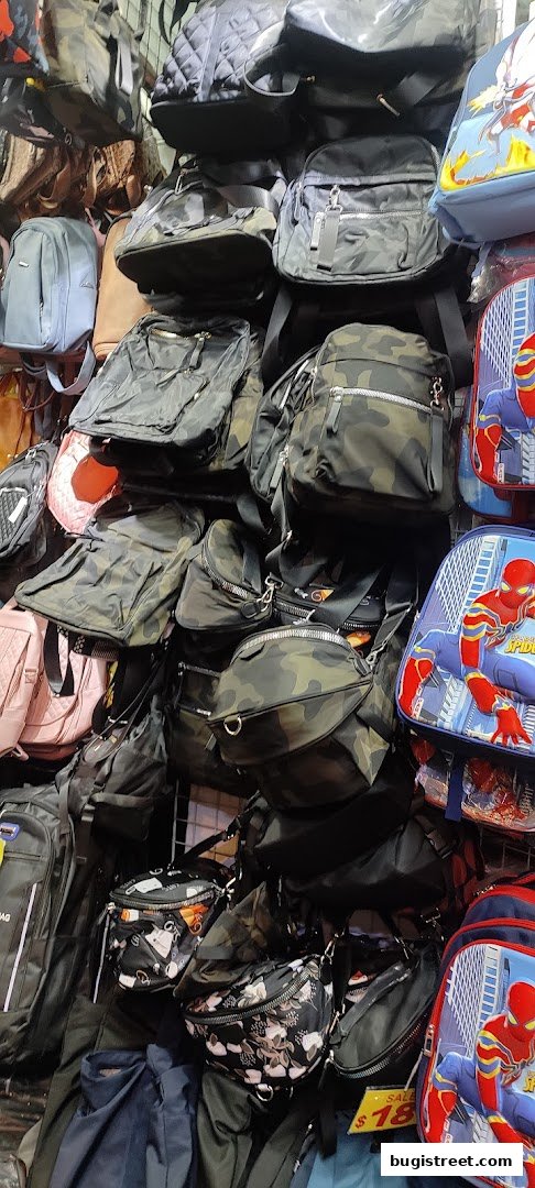 A display of various bags, including backpacks, crossbody bags, and fanny packs, in different colors and patterns.