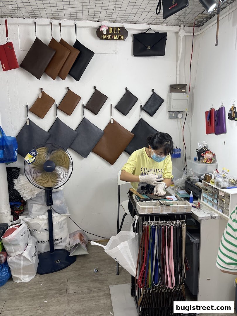 A person works on accessories in a shop filled with handbags and straps.
