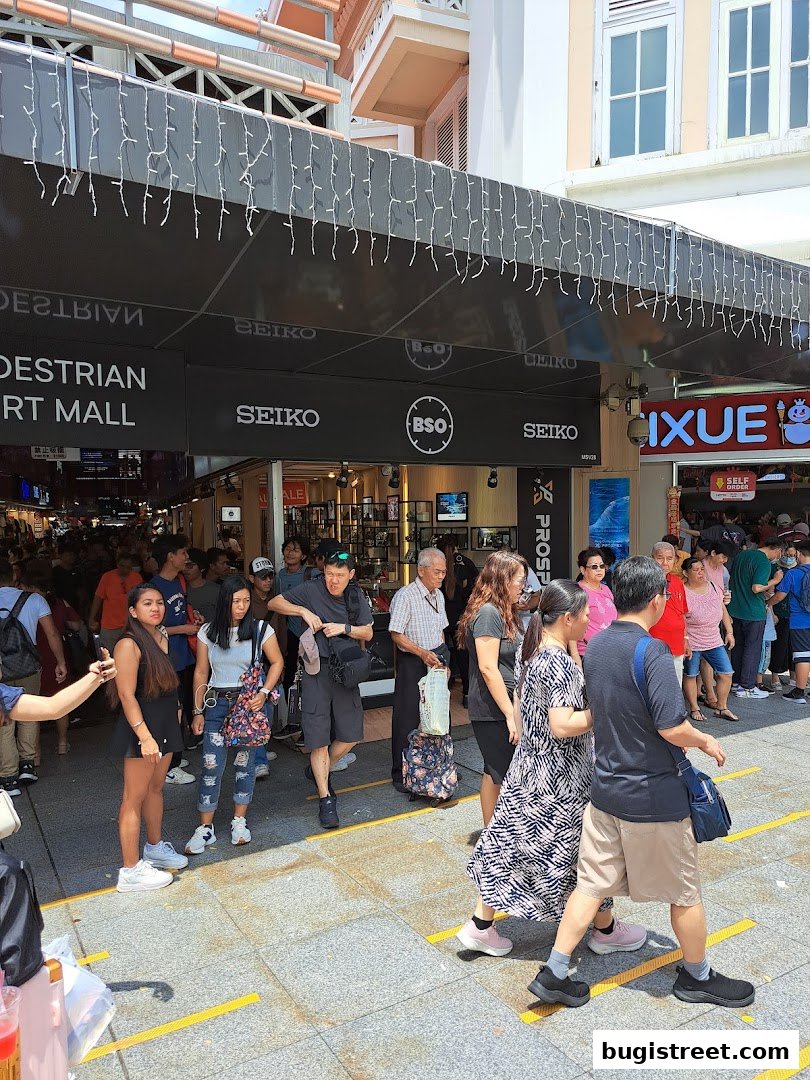 People walking past a BSO Watch store with Seiko branding and decorative lights.