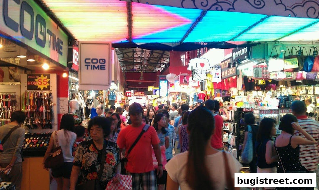 A busy street market with people browsing various stalls selling clothing and accessories.