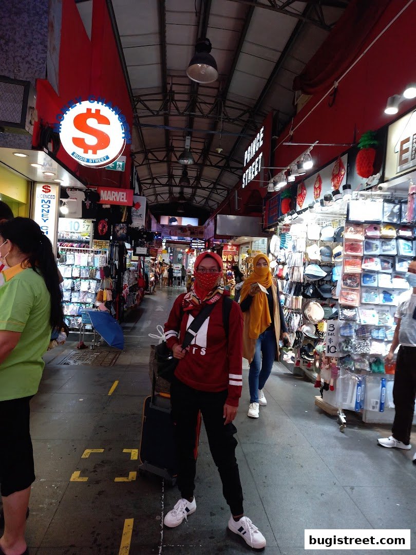 People walking through a busy street market with various stalls selling merchandise.