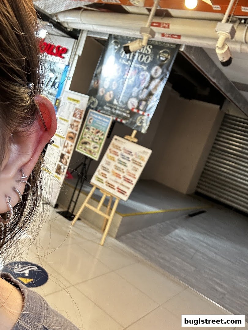 A person's ear with piercings is shown next to a display of tattoo and piercing services.