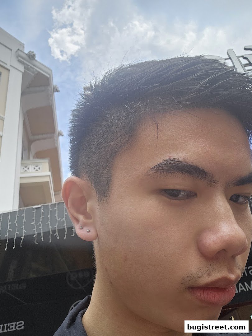 A close-up of a person's ear with multiple piercings, with a building and sky in the background.