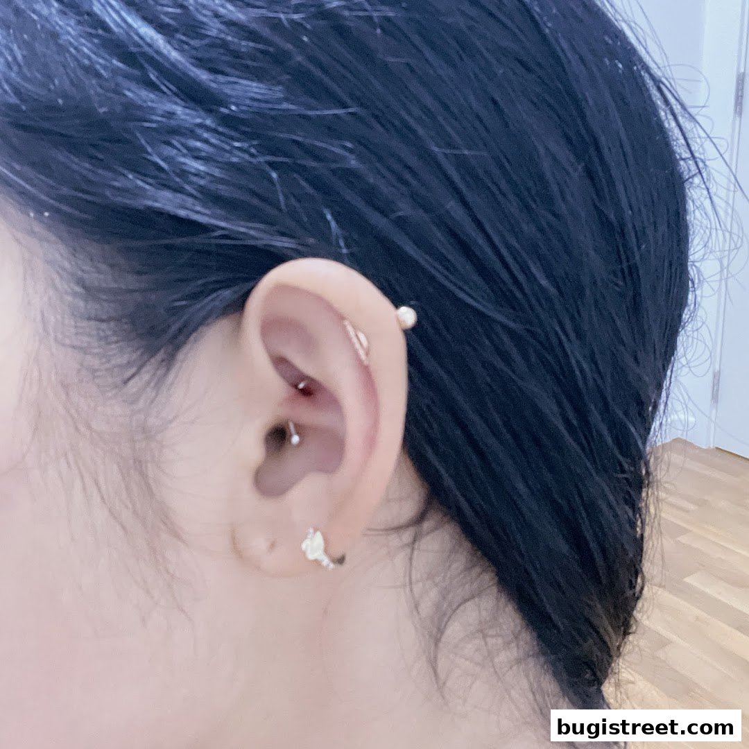 Close-up of a person's ear with multiple piercings, including an industrial and a daith.