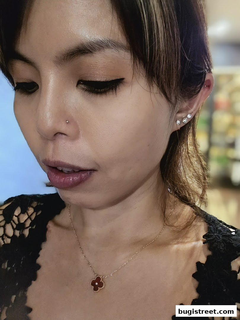 A close-up of a woman with a nose piercing, earrings, and a clover pendant necklace.