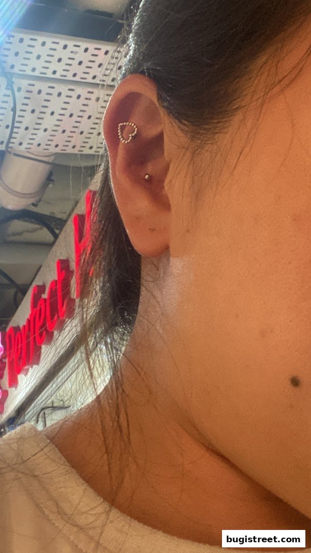 Close-up of a person's ear with a heart-shaped piercing and a second stud piercing.