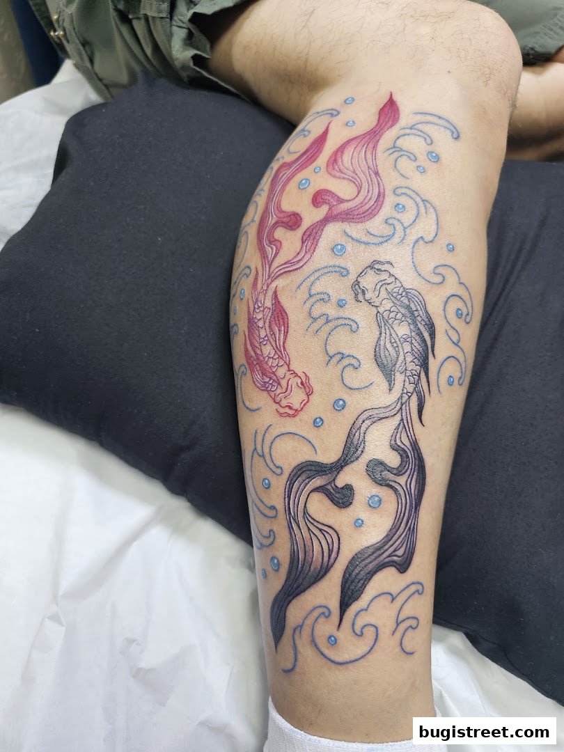 A close-up of a leg with a new tattoo of two koi fish swimming amidst waves.