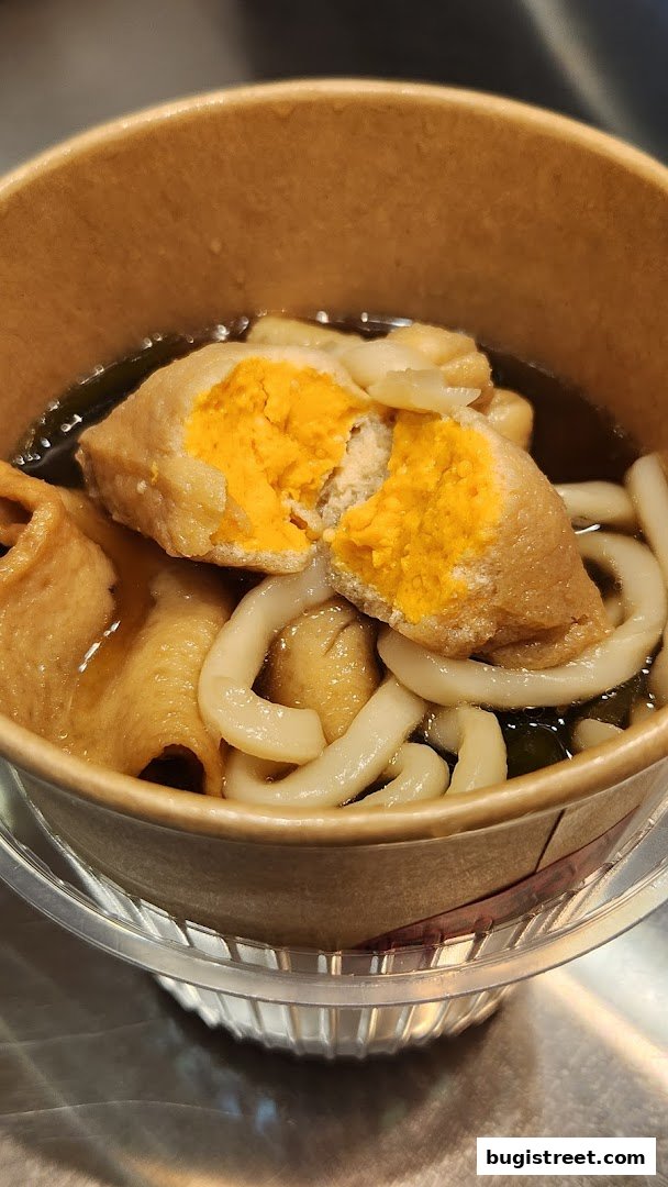 A close-up of a bowl of Oden with udon noodles and a stuffed fish cake.