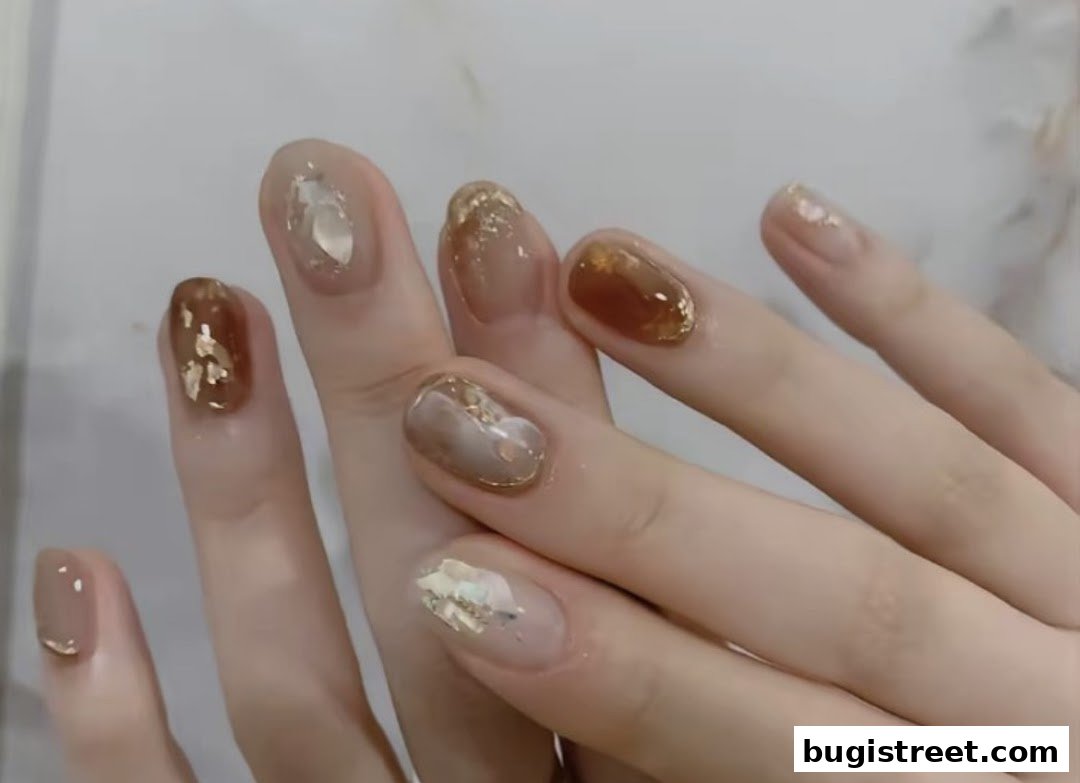 Close-up of hands with elegant, glossy nails featuring gold leaf and brown accents.