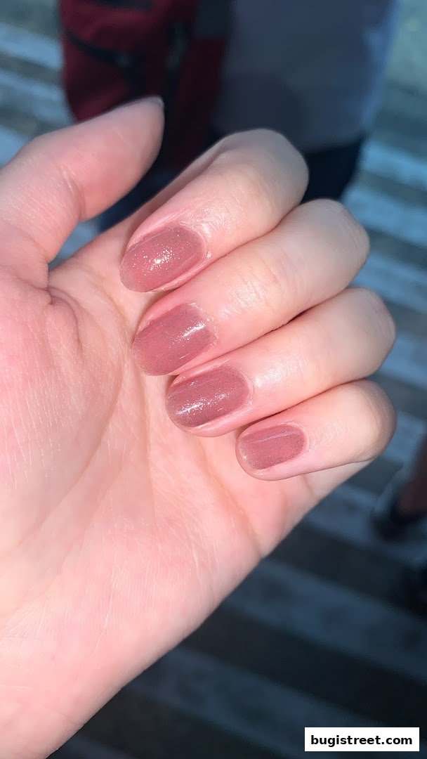 A close-up shot of a hand with perfectly manicured nails painted in a shimmery rose gold polish.