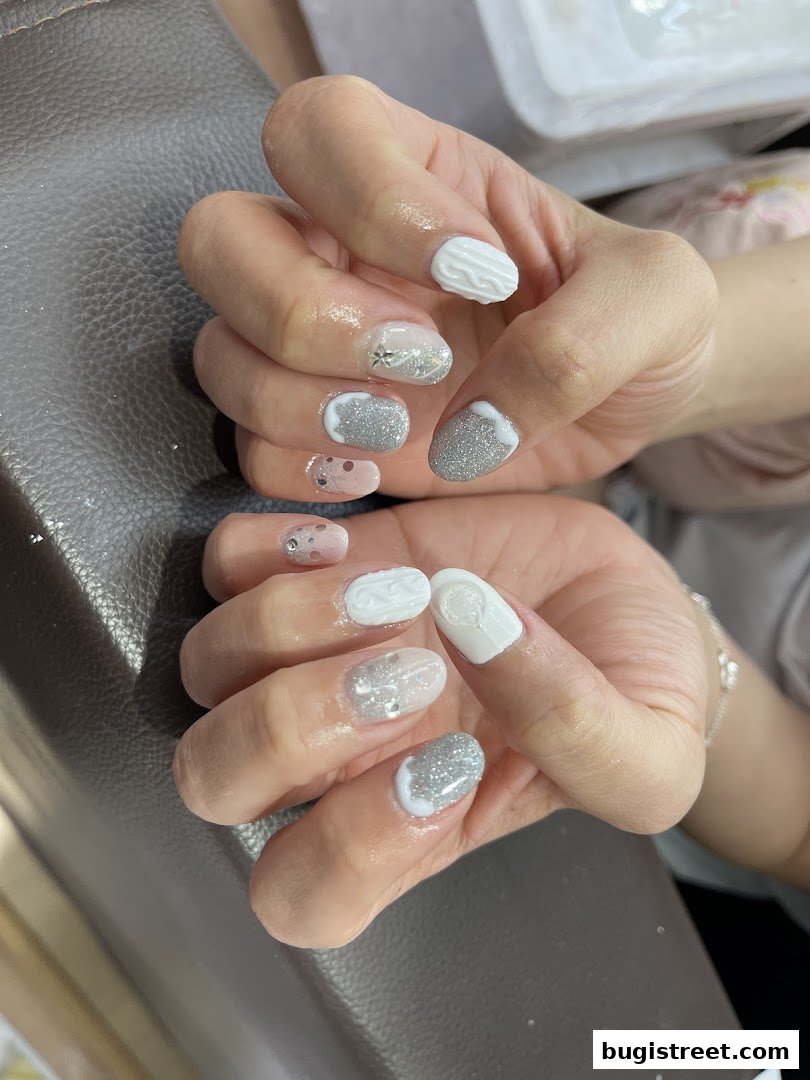Close-up of hands with intricate white and silver nail designs, featuring glitter and textured patterns.