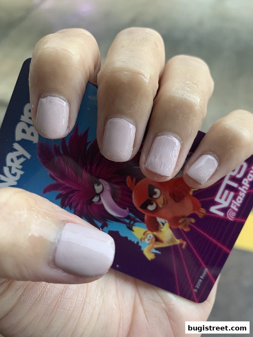 A close-up of a hand with light pink polished nails holding a card with Angry Birds characters.