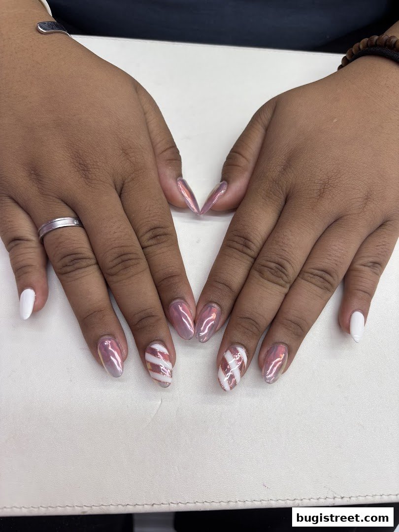 A close-up of hands with beautifully manicured nails featuring white and pink chrome designs.