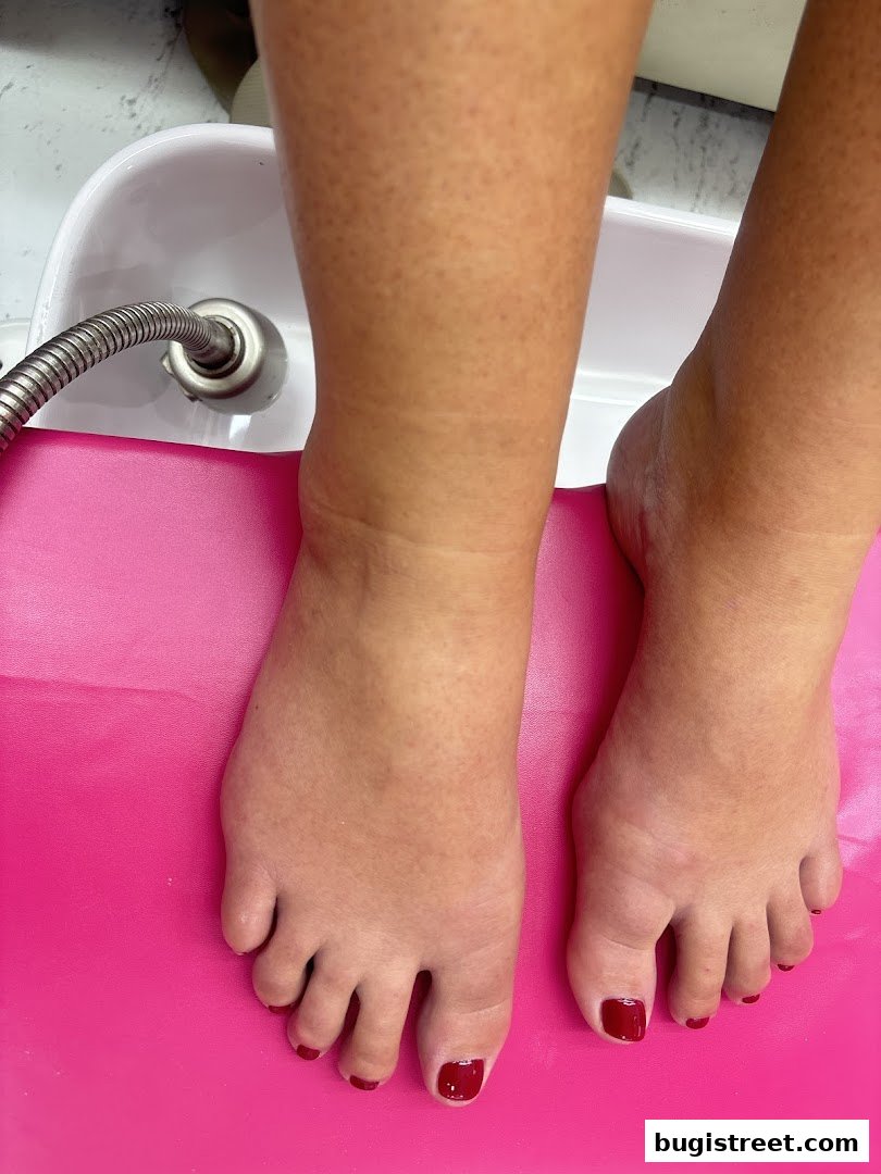 Close-up of feet receiving a pedicure with dark red nail polish.