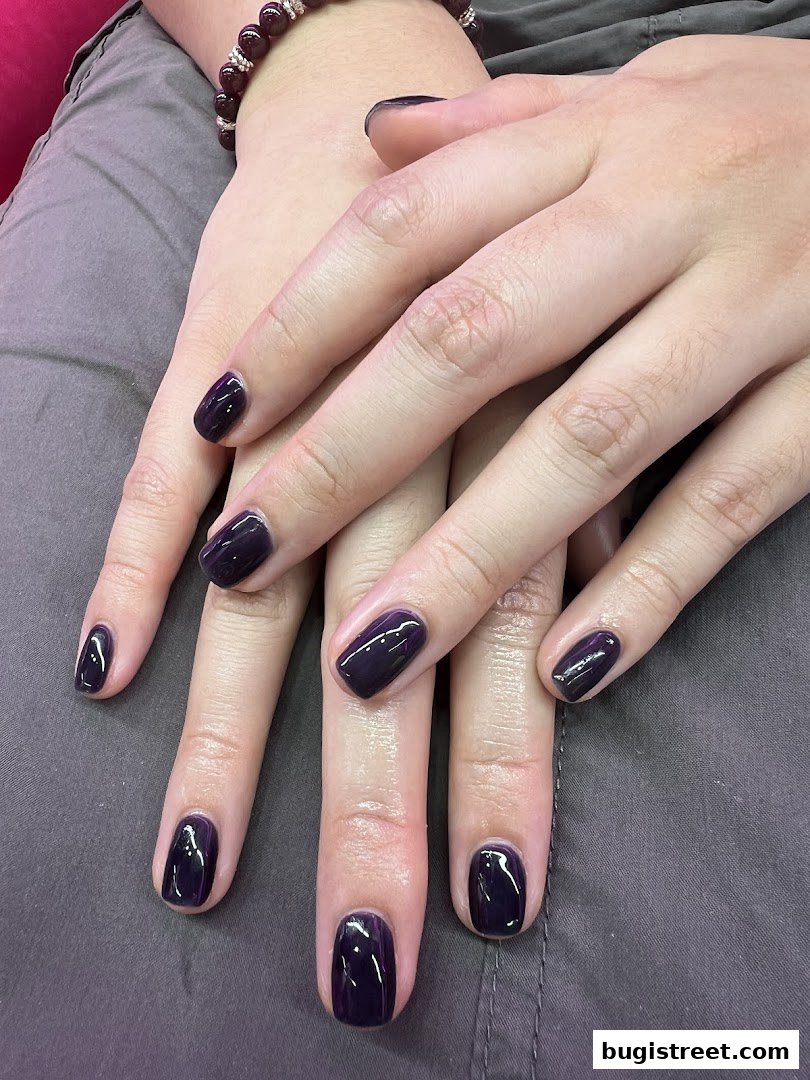 A close-up shot of hands with perfectly manicured, dark purple gel nails.