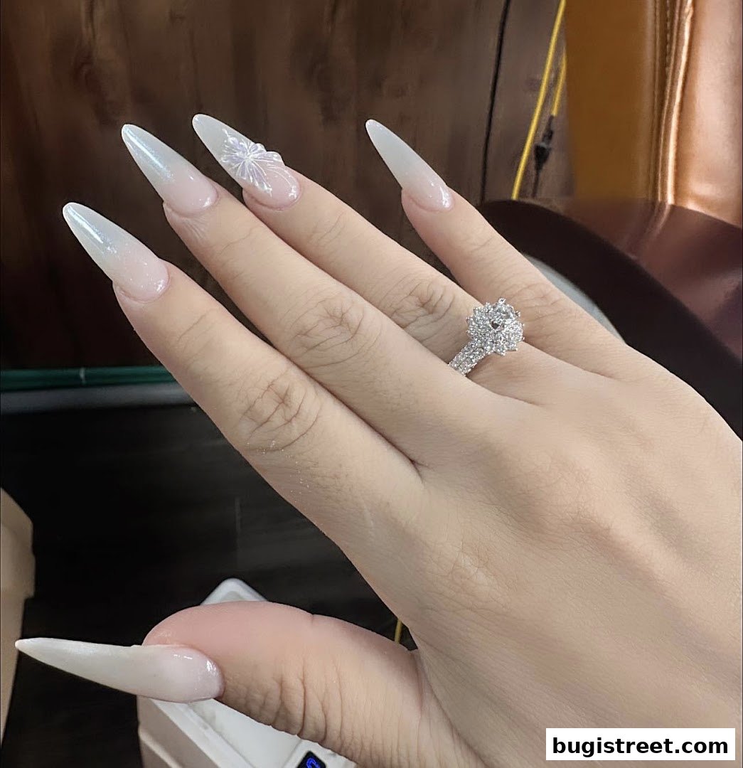A hand with long, elegant, stiletto-shaped nails adorned with a delicate butterfly design and a sparkling ring.