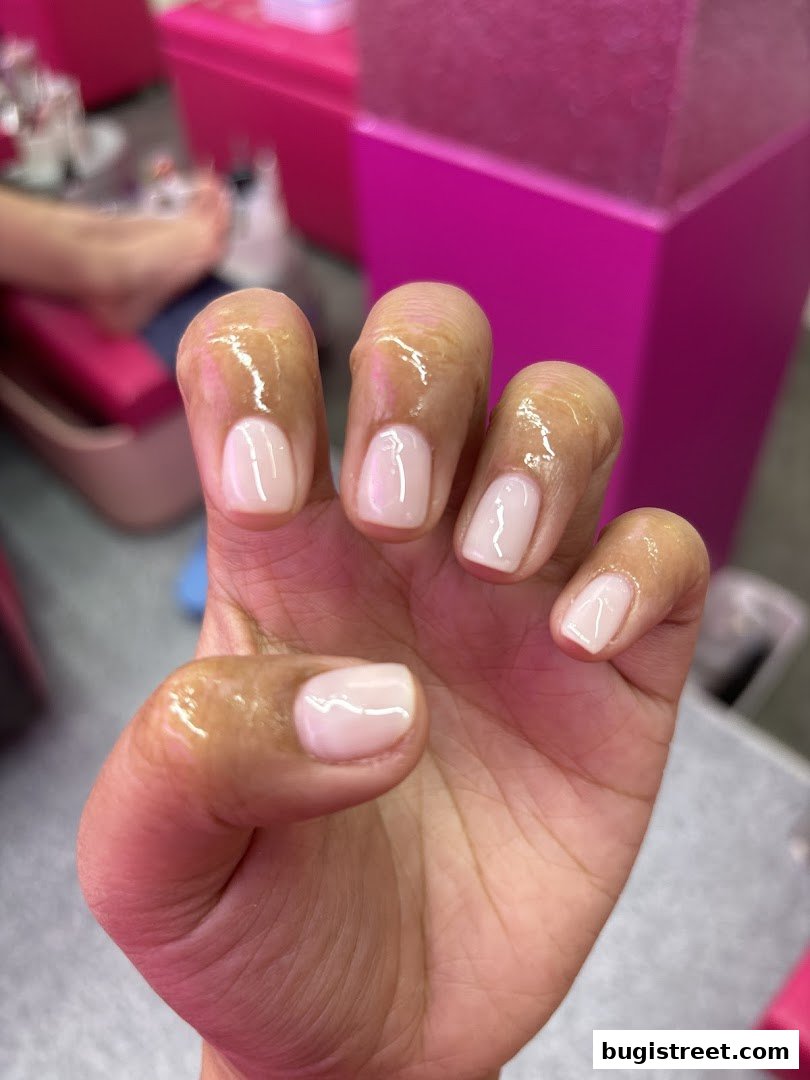 A close-up of a hand with freshly painted, light pink nails and cuticle oil.