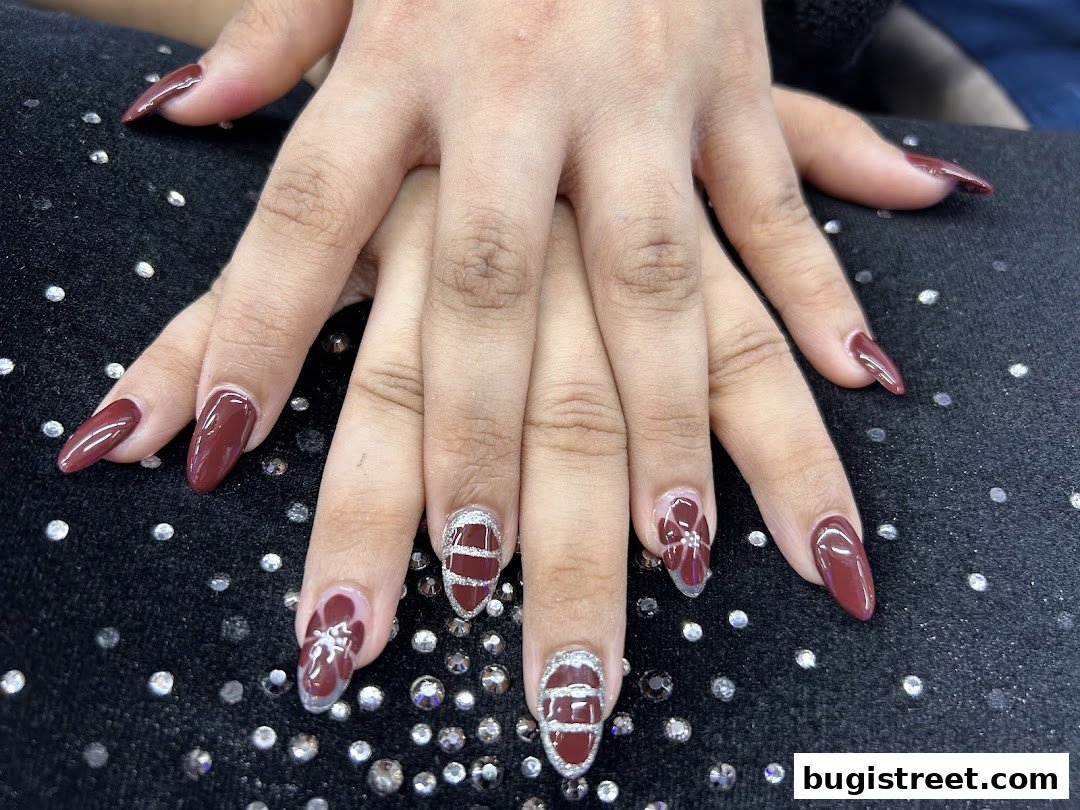 Close-up of hands with beautifully manicured nails featuring a deep red polish and intricate designs.
