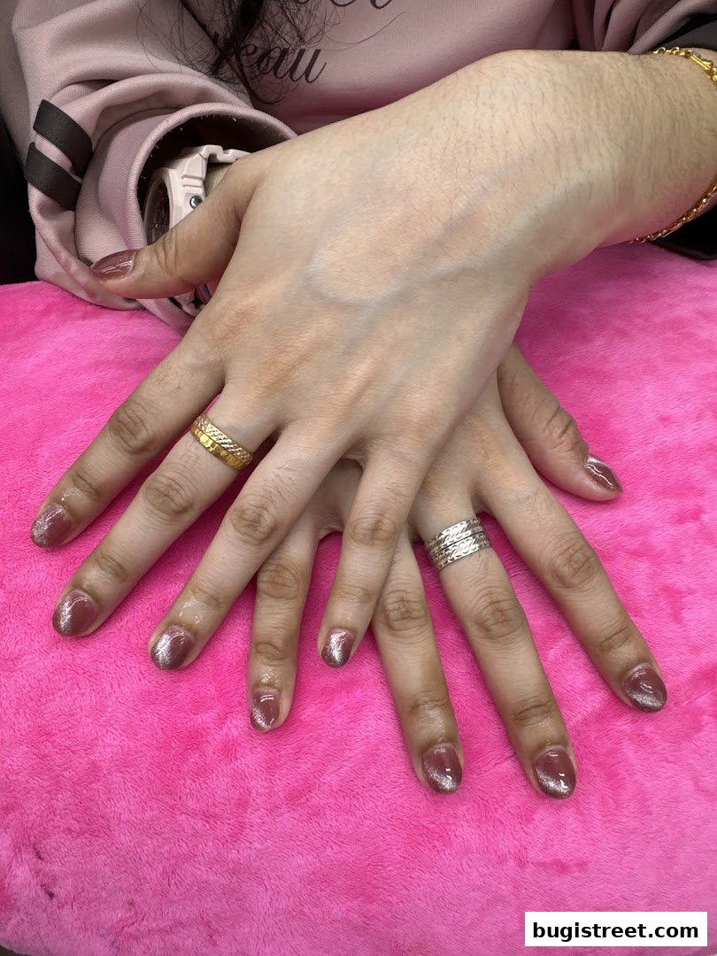 Close-up of hands with beautifully manicured nails and rings on a pink surface.