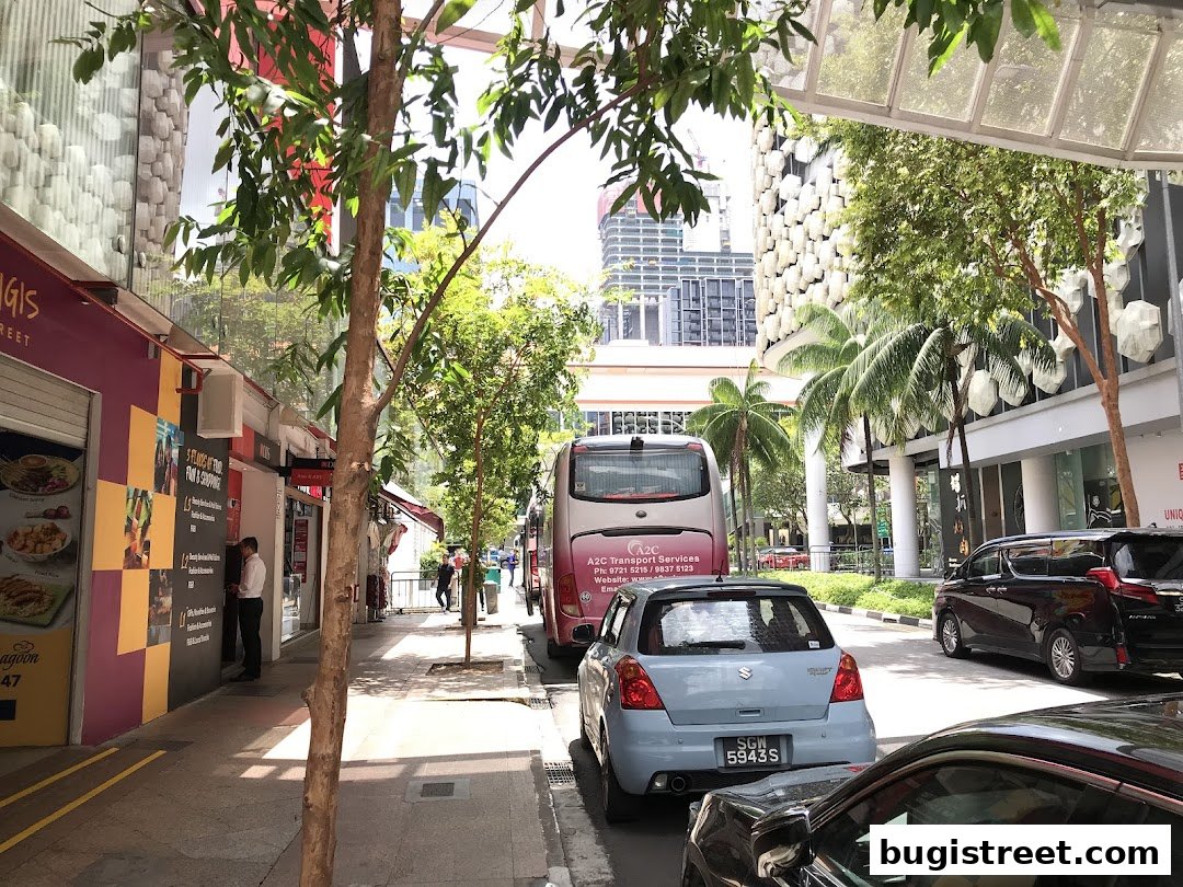 Street view of shops and an ATM with cars and a bus parked nearby.