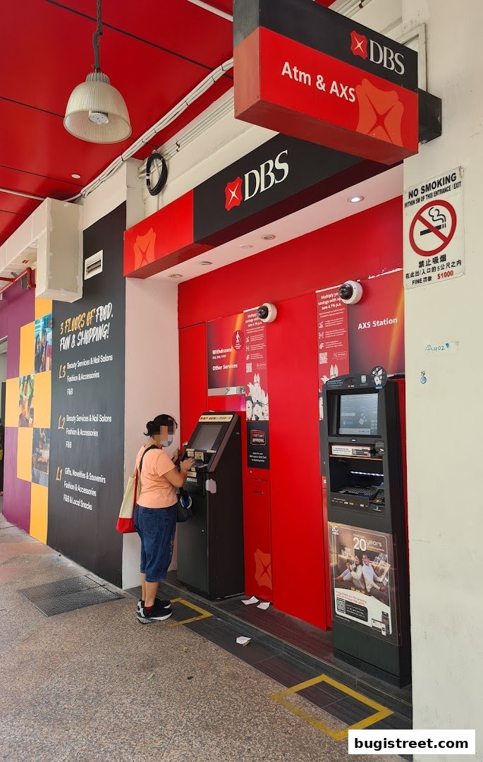 A person uses a DBS ATM and AXS machine at a street-level entrance.